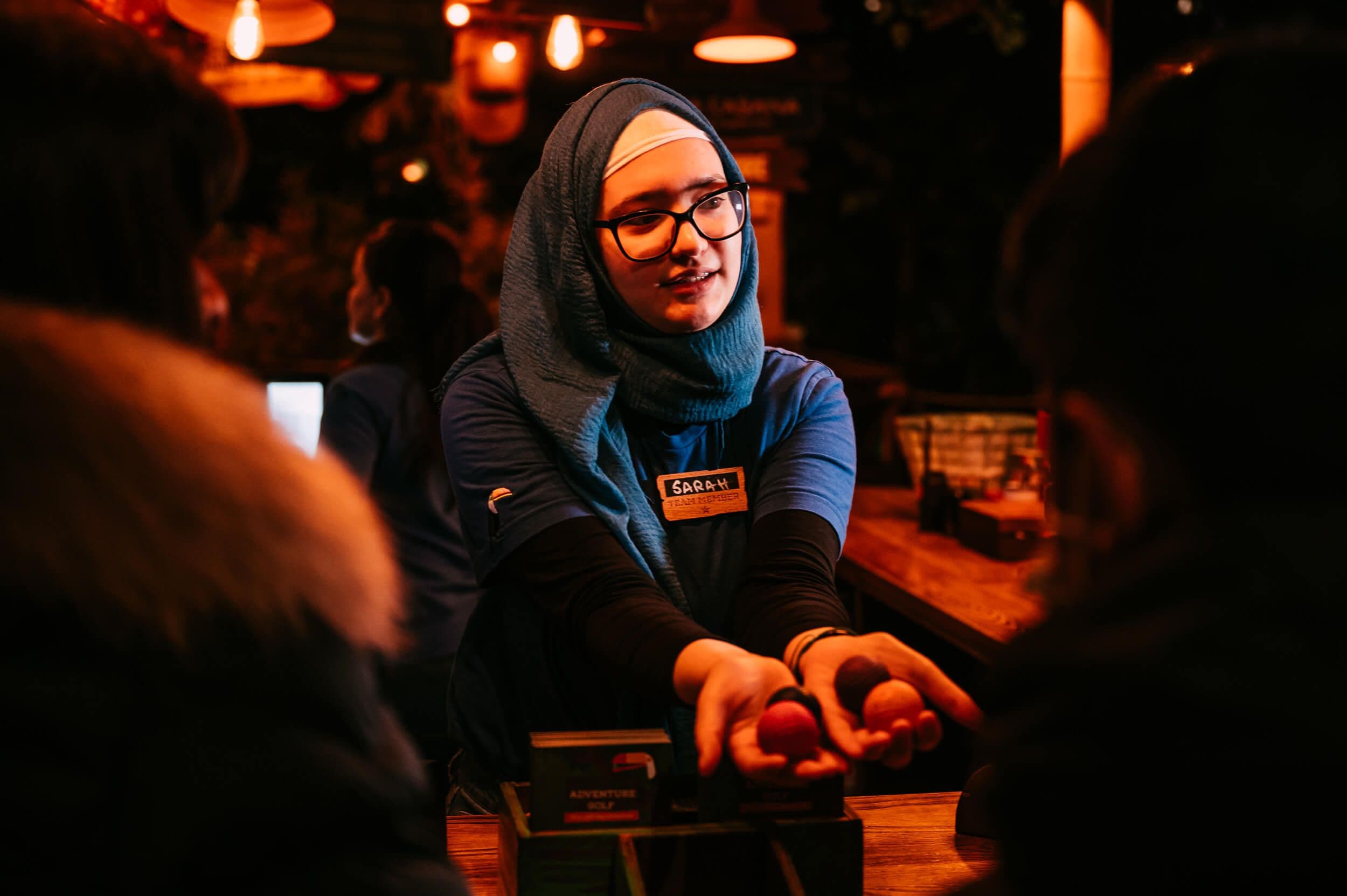 Helpful Treetop Golf visitor guide with blue headscarf handing players their mini golf balls.